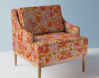 May include: A floral armchair with a white background and orange, pink, and yellow flowers. The chair has a wooden frame and legs.