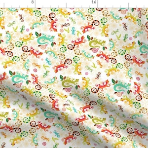 May include: A white fabric with a repeating pattern of colorful lizards and swirls. The lizards are in various shades of green, blue, orange, and yellow. The swirls are in shades of green, blue, and brown.