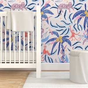 Pode incluir: Um berço branco com um cobertor branco dentro, contra um papel de parede rosa e azul com tema de selva. O papel de parede apresenta macacos rosa e azuis, leopardos rosas, palmeiras azuis e pássaros rosas.