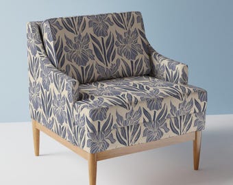 May include: Armchair upholstered in fabric with a blue and cream floral design. The chair has a wooden frame and legs. The floral pattern features iris flowers and leaves.