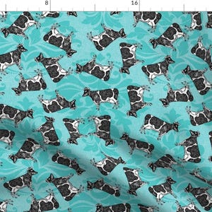 May include: A turquoise blue fabric with a repeating pattern of black and white cows. The cows are in a variety of poses, some are lying down, some are standing, and some are jumping. The fabric has a damask-like background pattern.