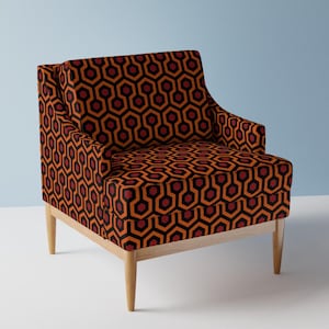 Peut inclure: Un fauteuil marron avec un motif géométrique dans des tons de rouge, orange et noir. Le fauteuil a des pieds en bois.