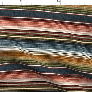 Puede incluir: Una tela con un patrón de rayas horizontales con bandas de azul oscuro, verde oliva, naranja óxido y blanco crema. El diseño tiene una apariencia texturizada con líneas finas de anchos variables que recorren la longitud del material.