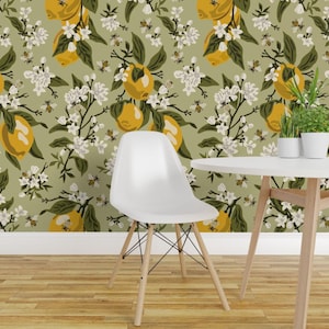 May include: A white moulded plastic chair with four light wood legs and black metal cross-bracing, positioned against a sage green wallpaper featuring a repeating pattern of yellow lemons, white blossoms, dark green leaves, and small bees.