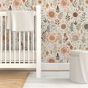 May include: A white crib with a white blanket inside, a white laundry basket, and a wall with a beige and brown wallpaper featuring a repeating pattern of suns and leaves.