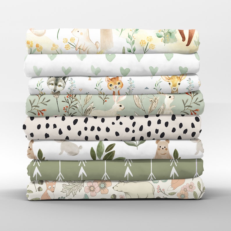 Puede incluir: Una pila de diez paneles de tela con diferentes estampados de animales del bosque y temas de la naturaleza. Los estampados incluyen zorros, ciervos, conejos, osos, lobos y patrones florales. Los paneles son en tonos de verde, blanco y marr&oacute;n.