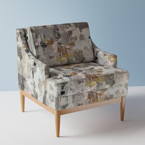 Könnte beinhalten: Ein grauer Sessel mit geometrisch gemustertem Bezug und Holzbeinen. Der Sessel hat eine hohe Rückenlehne und eine breite Sitzfläche.