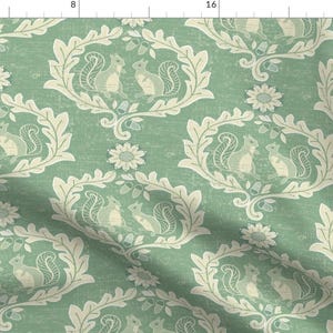 May include: A green fabric with a repeating pattern of squirrels and floral designs. The squirrels are in a light brown color and the floral designs are in a cream color.