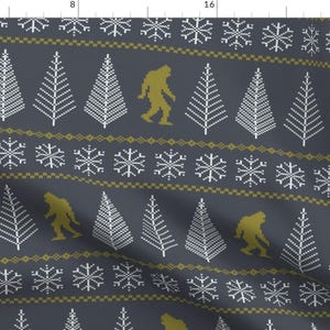May include: A dark blue fabric with a repeating pattern of white Christmas trees, yellow snowflakes, and yellow Bigfoot figures walking across the fabric.