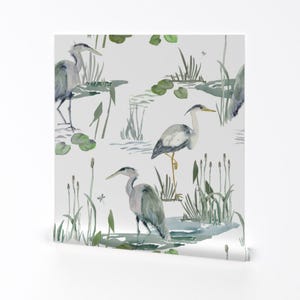 以下が含まれることがあります： 白い背景に、水彩画で描かれた灰色のサギが緑色のスイレンと葦のある池に立っているシームレスなパターンです。