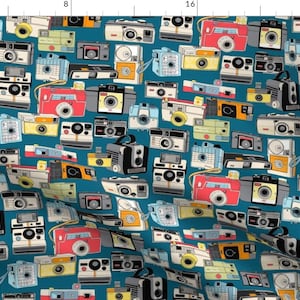 May include: A teal blue background with a repeating pattern of vintage cameras in various colours and styles. The cameras are drawn in a cartoon style and include a variety of shapes and sizes.