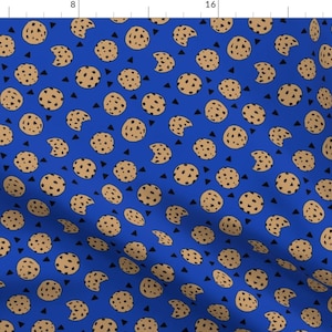 Pode incluir: Um tecido azul com um padrão repetido de biscoitos com gotas de chocolate castanho-claro e triângulos pretos. Alguns biscoitos têm uma mordida. Os biscoitos estão espalhados pelo tecido.