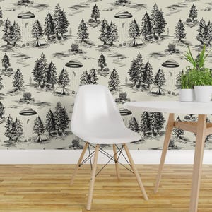 May include: Wallpaper featuring a repeating black and white ink-style illustration of a forest landscape with camping tents and flying saucers beaming light down. A white molded plastic chair with wooden legs sits in front of the patterned wall.
