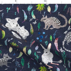 Può includere: Un tessuto blu navy con un motivo ripetuto di vari animali australiani, tra cui un koala, un bandicoot, un bilby e un quoll. Gli animali sono illustrati in uno stile fantasioso con accenti bianchi e grigi. Lo sfondo è blu scuro con fogliame verde e bianco.