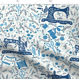 May include: A white fabric with a blue and white pattern of sewing machines, needles, buttons, thread spools, thimbles, scissors, and floral sprigs.