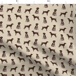 May include: A beige fabric with a repeating pattern of brown German Shorthaired Pointer dogs in various poses. The dogs are silhouetted and appear to be running, sitting, and standing.