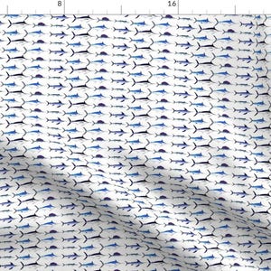 Op de afbeelding: Een witte stof met een herhalend patroon van blauwe en zwarte marlijn vissen. De vissen kijken allemaal dezelfde kant op en zijn in een verspringend patroon gerangschikt.
