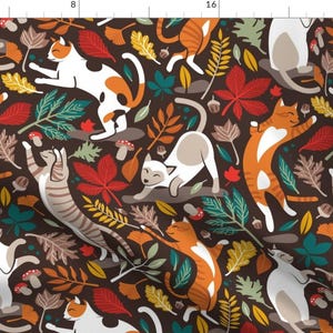 May include: A fabric pattern with cartoon cats amongst autumn leaves, acorns, and mushrooms. The cats are orange, white, and grey. The leaves are red, green, and yellow on a dark brown background.