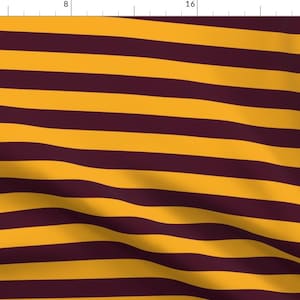 May include: A fabric with alternating horizontal stripes of maroon and gold. The fabric is slightly wrinkled and has a soft, textured appearance.