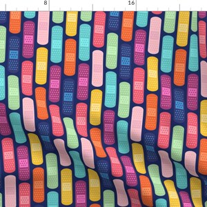 May include: Fabric with a repeating pattern of colorful bandages in shades of pink, orange, yellow, green, and blue on a navy blue background. The bandages have a dotted texture.