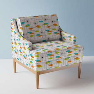 May include: Mid-century modern armchair with a light wood frame and legs. The chair is upholstered in a white fabric with a colorful pattern of orange, teal, and green ovals, and black starbursts and lines.