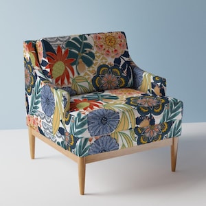 Puede incluir: Un sillón con estampado floral sobre un fondo blanco y flores de colores. El sillón tiene un marco y patas de madera.