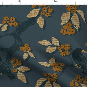 Op de afbeelding: Een donkerblauwe stof met een herhalend patroon van zwarte vogels, oranje bloemen en tekst uit een boek. De vogels zitten op takken met bladeren. De tekst is vervaagd en lijkt uit een oud boek te komen.