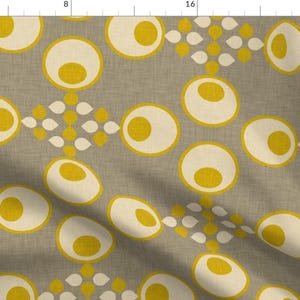May include: A beige fabric with a repeating pattern of yellow and white circles. The circles are arranged in a staggered pattern, with the yellow circles in the centre of the white circles.