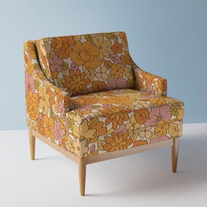 May include: A vintage-style armchair with a floral pattern in shades of orange, yellow, and pink. The chair has a wooden frame and tapered legs. The upholstery features a large-scale floral design, creating a retro aesthetic.