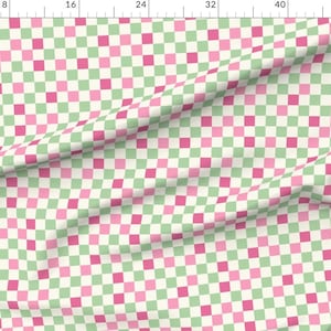 May include: Fabric with a repeating checkerboard pattern. The pattern features squares in light green, pink, and off-white. The fabric is draped, creating soft folds and shadows across the surface.