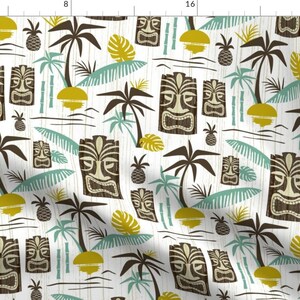 Op de afbeelding: Een witte achtergrond met een herhalend patroon van bruine tiki-maskers, groene palmbomen, gele ananas en blauwe en groene bladeren. Het patroon is een retro-geïnspireerd ontwerp.
