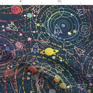 May include: A dark blue fabric with a colorful space-themed pattern. The pattern includes rockets, planets, stars, and swirling galaxies. The fabric is perfect for crafting projects, quilting, and home decor.