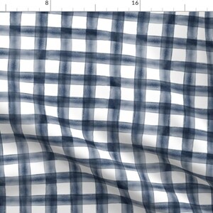 May include: A white fabric with a blue and white watercolor gingham pattern. The fabric has a subtle, faded look, giving it a vintage feel.