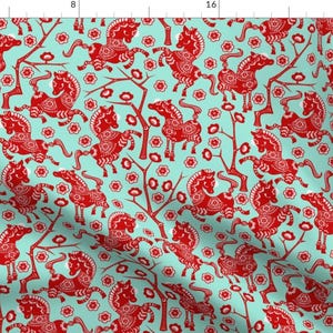 Puede incluir: Tela estampada con un patrón repetitivo de caballos rojos y elementos florales sobre un fondo azul claro. Los caballos están estilizados con detalles intrincados, y el diseño tiene una estética de inspiración asiática.