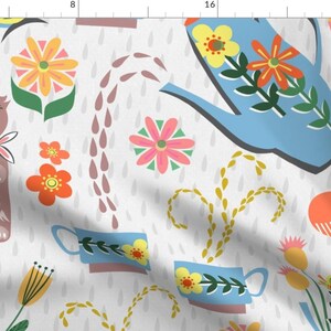 May include: Fabric with a whimsical pattern featuring a brown cat, blue watering can, flowers, and teacups on a white background. The design includes orange, yellow, and pink floral elements, along with stylized rain drops.