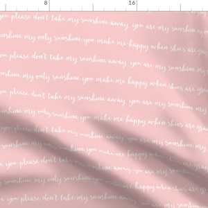 Op de afbeelding: Een roze stof met een wit, herhalend patroon van de tekst "You are my sunshine, my only sunshine, you make me happy when skies are gray, you'll never know dear, how much I love you, please don't take my sunshine away".