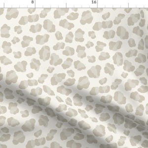 May include: A white fabric with a beige leopard print pattern. The fabric has a subtle texture and a soft, flowing drape.