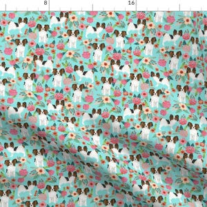 Pode incluir: Um padrão sem costura apresentando um cão da raça papillon branco e marrom com orelhas marrons e um rosto branco e preto. O cão está rodeado de flores rosa, brancas e amarelas sobre um fundo azul turquesa.