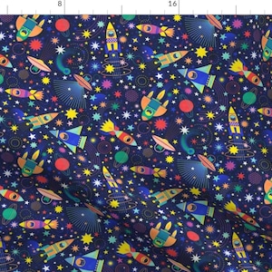 May include: A fabric featuring a repeating pattern of colourful rockets, planets, stars, and other space-themed elements on a dark blue background. The rockets are in various colours, including yellow, orange, and blue.