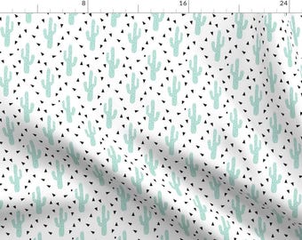 May include: A white fabric with a repeating pattern of light green cacti and small black triangles.