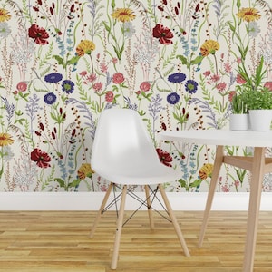 May include: A white molded plastic chair with four light wood legs stands before a wall covered in wallpaper featuring a botanical pattern of red poppies, yellow daisies, purple cornflowers, and green grasses on a cream-colored background.