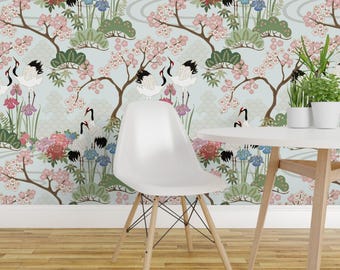 May include: A white moulded plastic chair with four light wood legs and black metal cross-bracing, positioned in front of a light blue wallpaper featuring a repeating pattern of white cranes, pink cherry blossoms, green pine trees, and flowers.