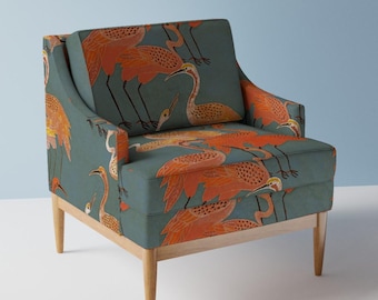 May include: An upholstered armchair with a teal background and a repeating pattern of orange and yellow birds. The chair has light-colored wooden legs and armrests. The birds are depicted in a stylized, artistic manner.