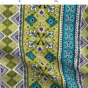 Op de afbeelding: Een stof met een herhalend patroon van geometrische vormen in tinten groen, blauw, wit en paars. Het patroon doet denken aan traditionele tribale kunst.