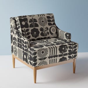 May include: A patterned armchair with a beige background and black floral designs. The chair has a wooden frame and legs. The design includes various stylized flowers and geometric shapes. The chair is a comfortable seating option for a living room or bedroom.