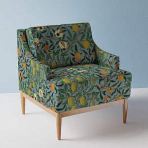 Peut inclure: Un fauteuil avec un revêtement en tissu bleu clair présentant un motif répétitif de fruits jaunes et orange, de fleurs blanches et de feuilles vertes. Le fauteuil possède un dossier carré, deux accoudoirs et quatre pieds en bois clair.