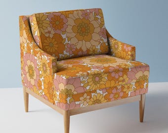 May include: A floral patterned armchair with a light wood frame and legs. The chair has a high back and a wide seat. The floral pattern is in shades of orange, yellow, pink, and white.