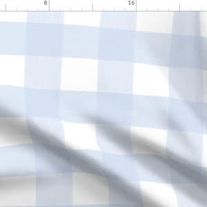 Op de afbeelding: Een lichtblauwe en witte gingham stof met een subtiele textuur. De stof is gevouwen en gedrapeerd, waardoor het patroon zichtbaar is.