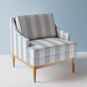 Op de afbeelding: Een fauteuil bekleed met een stof met verticale strepen in lichtblauw en gebroken wit. De stoel heeft een vierkante rugleuning, een dik zitkussen en vier taps toelopende houten poten in een natuurlijke lichtbruine afwerking.