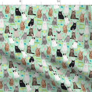 May include: A repeating pattern of cats wearing bunny ears on a light green background. The cats are in various poses and colors, including gray, brown, black, and white.